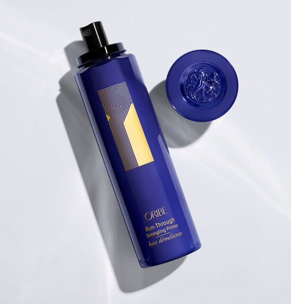 A bottle of Oribe Run-Through Detangling Primer lays on its side with removed cap nearby