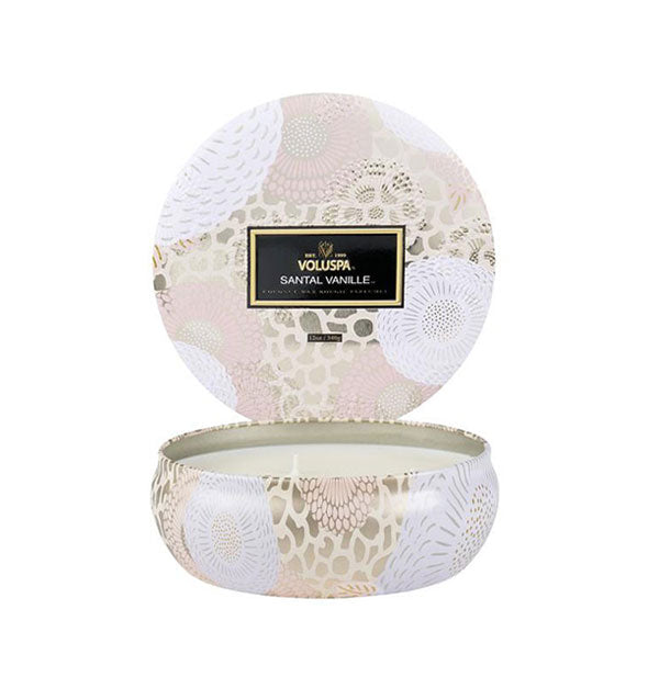 Round pastel pink, white, and gold floral patterned Voluspa Santal Vanille candle tin with lid removed and placed upright behind the tin