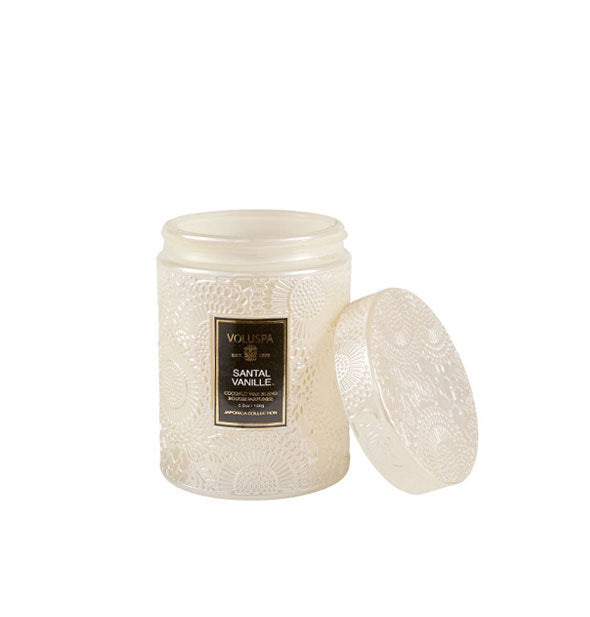 White embossed glass jar Voluspa candle with black label and embossed lid set to the side