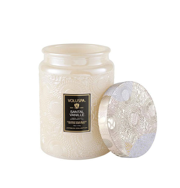 Pearlescent white embossed glass Voluspa Santal Vanille candle jar with whitish metallic tin lid removed and propped up alongside