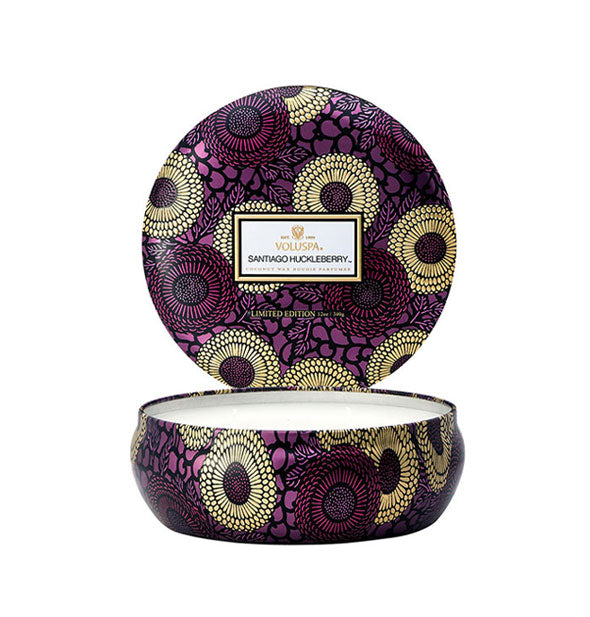 Round purple, gold, and black floral patterned Voluspa Santiago Huckleberry candle tin with lid removed and placed upright behind the tin