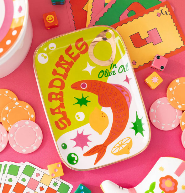 Sardines dish staged on a pink surface with pokes chips, playing cards, dice, and other items