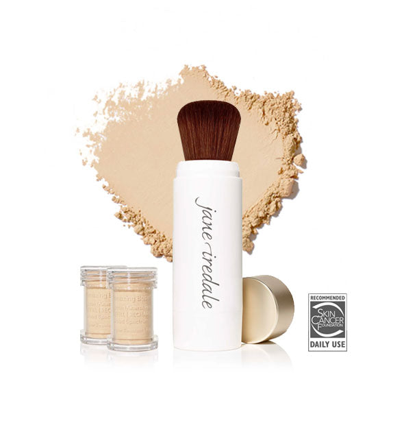 White Jane Iredale powder brush with gold cap removed and set to the side, two refill canisters nearby, and an enlarged product sample in the background in shade Satin