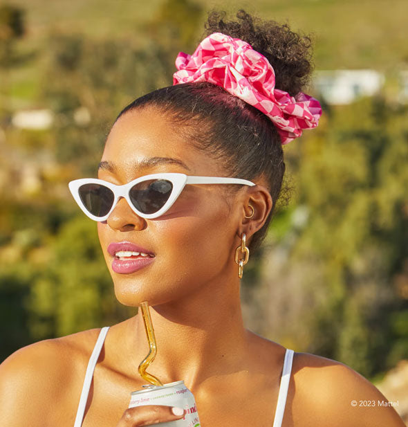 Model wears a pair of white cat-eye sunglasses and a pink checkered silk hair scrunchie in a topknot