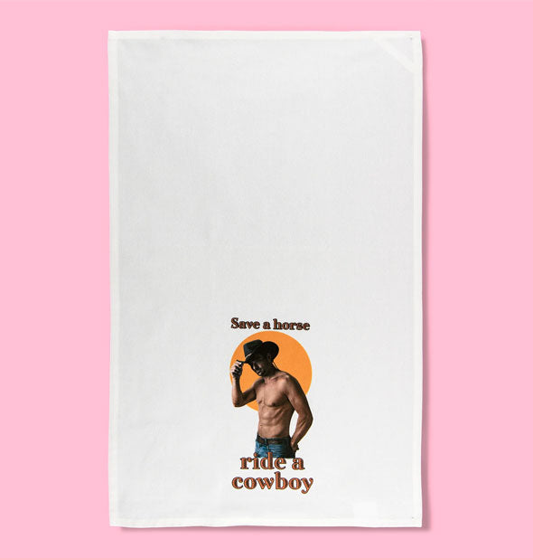 White dish towel on pink background featuring image of a shirtless man wearing jeans and touching the brim of his cowboy hat says, "Save a horse, ride a cowboy"