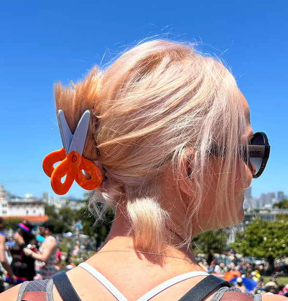 Model in a sunny outdoor setting wears a scissors claw clip in a swept-back hairstyle