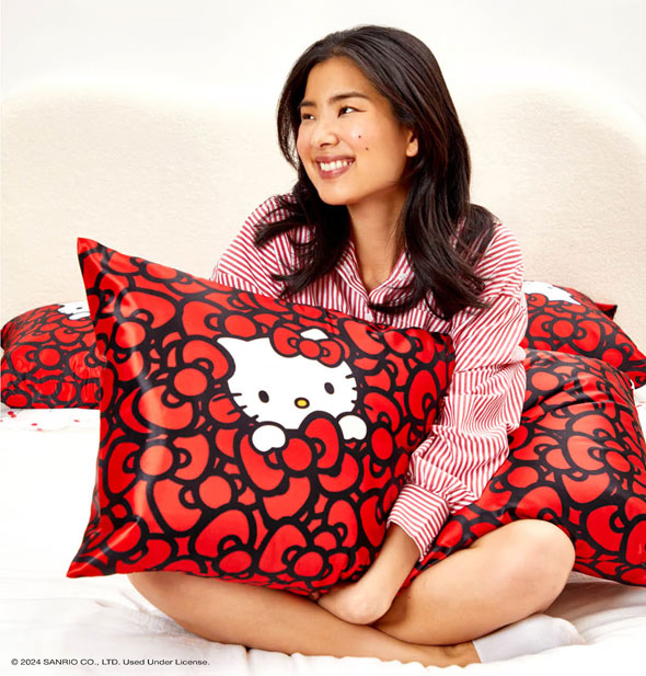 Smiling model hugs a king size pillow fitted with the Hello Kitty Bathes in a Sea of Bows satin pillowcase