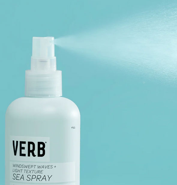 A fine mist of product is dispensed from a bottle of Verb Sea Spray against a blue backdrop