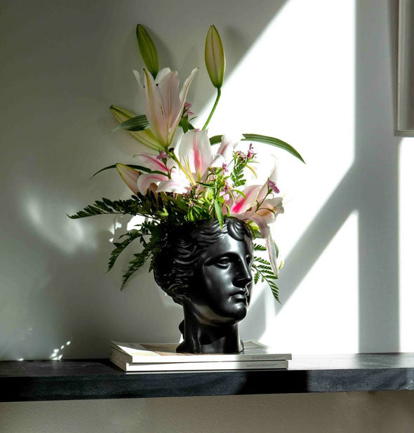 Selene goddess head vase holds an arrangement of fresh ferns and florals on a sunlit shelf