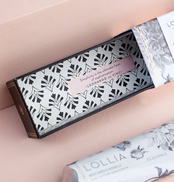 Opened Lollia handcreme box packaging features a patterned interior with printed quote by Leonardo da Vinci: "Simplicity is the ultimate form of sophistication."