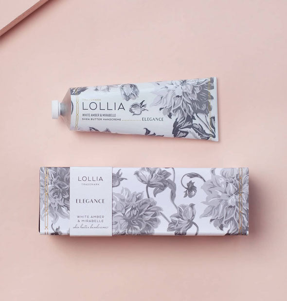Tube and box of Lollia Elegance White Amber & Mirabelle Shea Butter Handcreme on a pink surface are both designed with black and white floral patterning