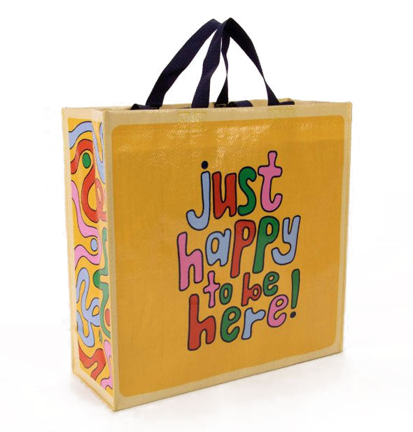 Square yellow shopping back with black top handles says, "Just happy to be here!" in colorful cartoonish lettering