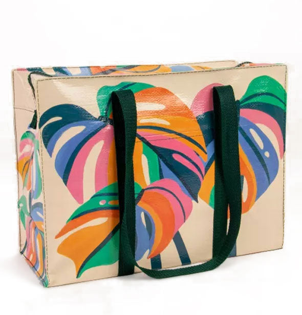 Cream-colored rectangular bag with dark green straps features illustrations of multicolored monstera leaves