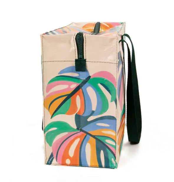 Cream-colored rectangular bag with dark green straps and zipper features illustrations of multicolored monstera leaves
