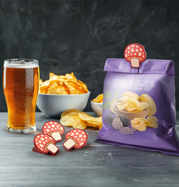 Set of four Shroommates mushroom bag clips staged on a tabletop with Black Truffle chips, glass of beer, and bowl of chips in the background
