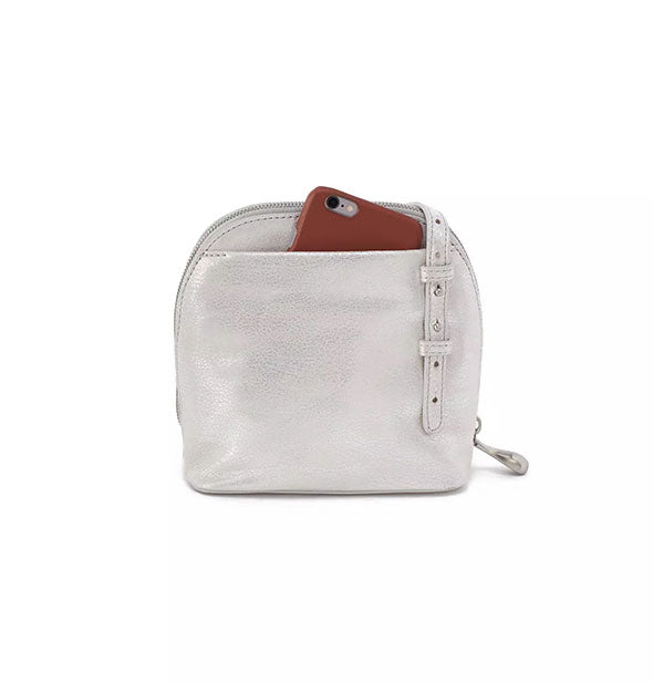 Reverse side of silver leather crossbody bag reveals strap attachment and exterior slip pocket out of which a phone is partially emerging