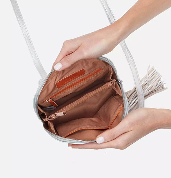 Model's hands hold open a silver leather crossbody bag to reveal its brown interior lining and pockets