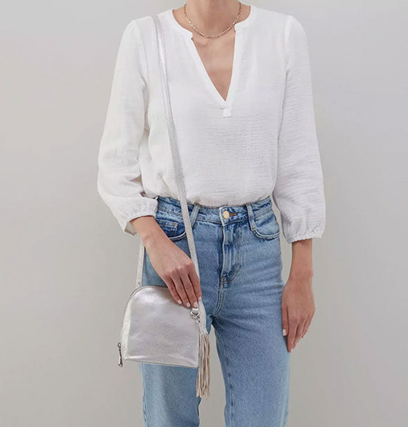 Model wearing jeans and a white shirt wears the silver leather Nash Crossbody purse over shoulder