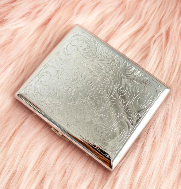 Rectangular silver cigarette case with ornate floral etching rests on pink fur