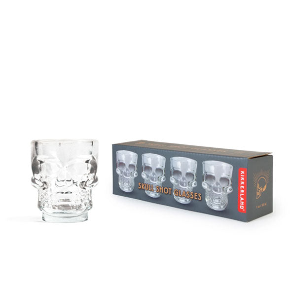 A clear skull-shaped shot glass from a set of four sits next to its gray box packaging