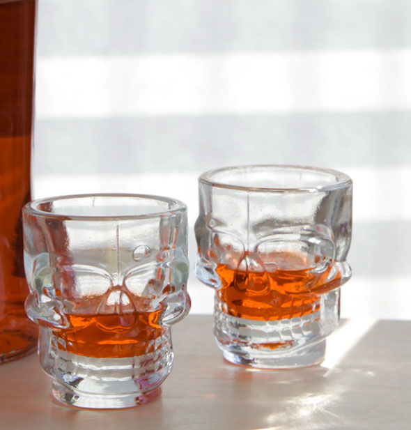 Two skull shot glasses hold some amber-colored liquid on a sunny tabletop