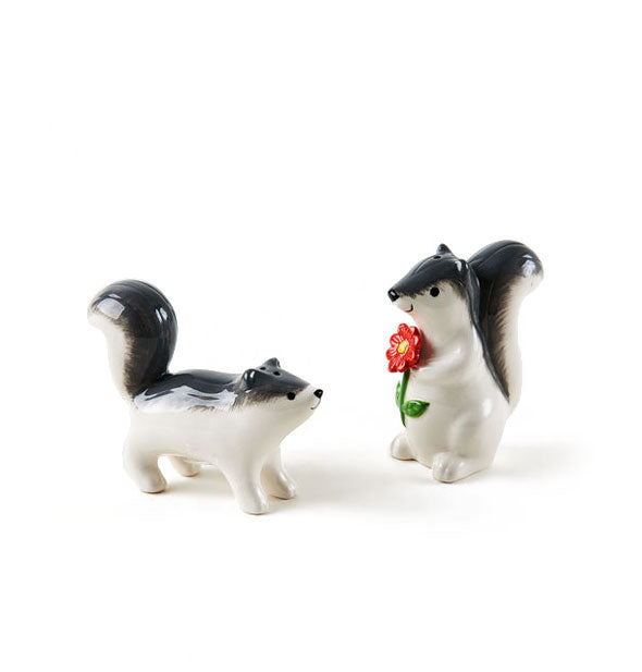 Set of ceramic skunk salt and pepper shakers—one is standing on all fours and the other is on hind legs and holding a red flower; both appear to be smiling