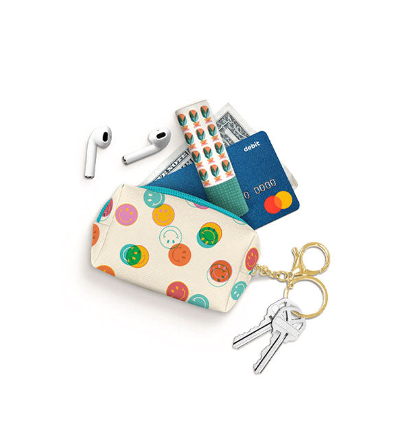 Contents spill out of a smiley face pouch: earbuds, lip balm, credit card, and dollar bill