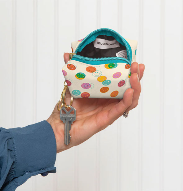 Model's hand holds a smiley face keychain pouch, squeezing it open slightly