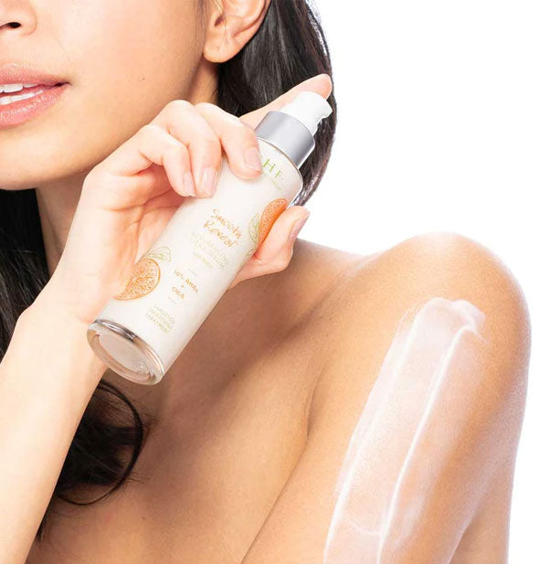 Model holds a bottle of FarmHouse Fresh Smooth Reveal Resurfacing Silky Serum in one hand while a thick streak of product has been applied to her opposite shoulder