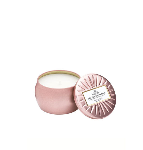 Metallic pink Sparkling Rosé Voluspa candle tin with lid featuring radial embossing set to the side