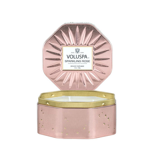 Octagonal pink speckled Voluspa Sparkling Rose candle tin with gold rim and a removed, radially embossed lid set upright behind the tin