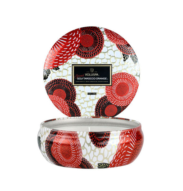 Round white, red, and black floral patterned Voluspa Goji Tarocco Orange candle tin with lid removed and placed upright behind the tin