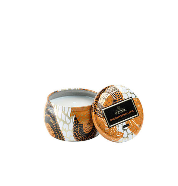 Unlit candle in a small, rounded tin with black, white, orange, and metallic design accents