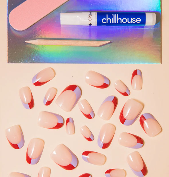 Contents of the Split the Bill Chill House press-on nail kit: Assortment of nails in varying sizes with a nude base and half red half lilac tip, pink nail file, wooden cuticle pusher, and glue tube