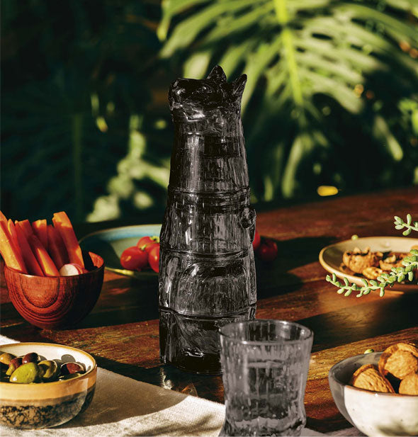 Stacked black cat glasses staged on a tabletop with food items