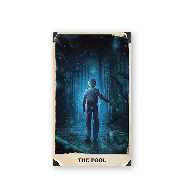 The Fool card from the Stranger Things Tarot Deck featuring moody illustration of a child in a blueish wooded area