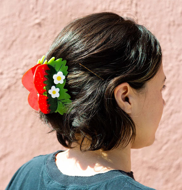 Model wears a hair clip designed to resemble two strawberries with green leaves and white flowers with yellow centers