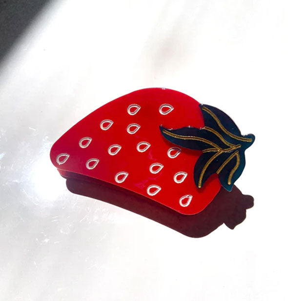 Hair clip designed and painted to resemble a red strawberry with white teardrop-shaped seeds and a green stem with gold line accents