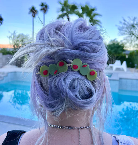 Model sitting poolside wears two olive trio hair clips in a messy updo