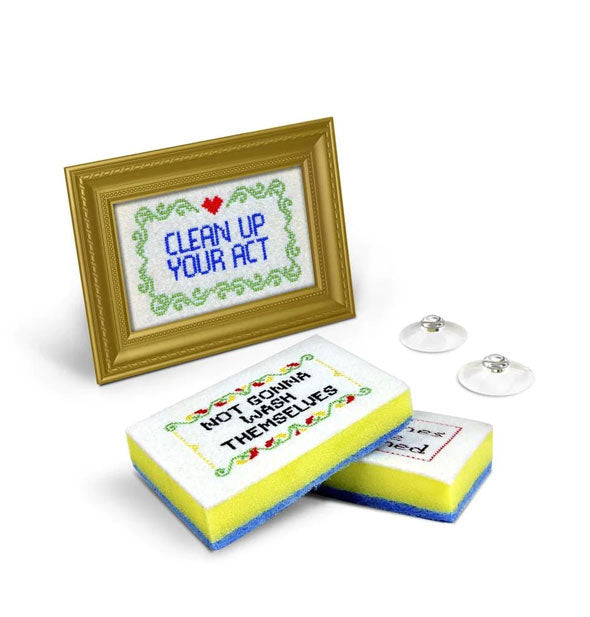 Dish sponges with cross-stitch artwork including the messages, "Clean up your act" and "Not gonna wash themselves" with gold frame and suction cups