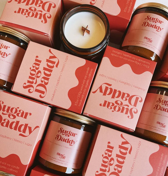 Collection of Sugar Daddy candle jars and boxes; one opened jar reveals its wooden X-shaped wick inside