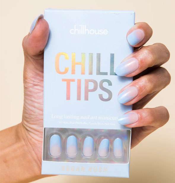 Model's hand wearing Chill House Sugar Rush blue-to-pink ombre Chill tips press-on nails holds a box of the same style
