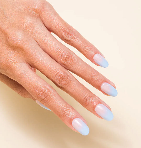 Model's hand wears a set of pastel blue-to-pink ombre press-on nails