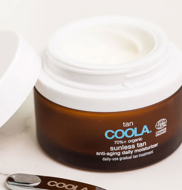 Pot of Coola Sunless Tan Anti-Aging Daily Moisturizer with removed lid and applicator resting alongside