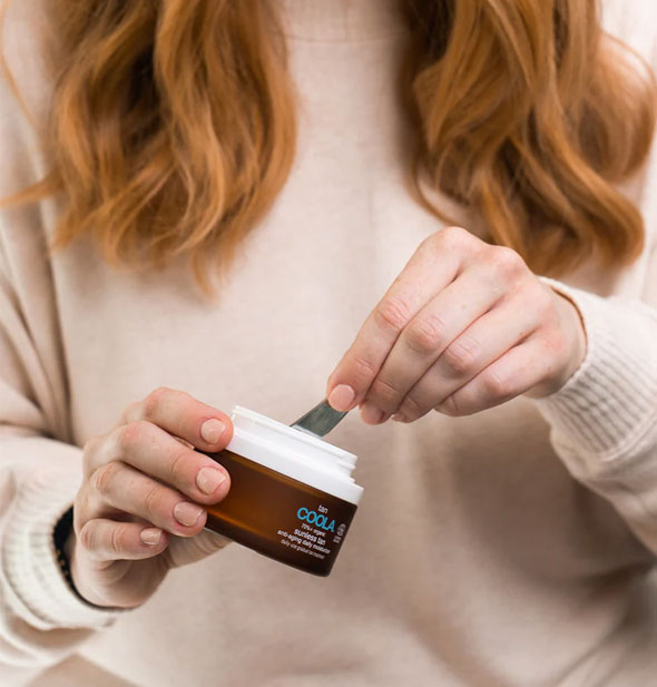 Model dips a product applicator into a open jar of Coola Sunless Tan Anti-Aging Daily Moisturizer