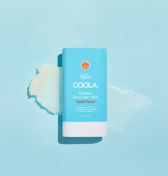 Stick of Coola Classic Sunscreen rests on a light blue surface with a smear of product