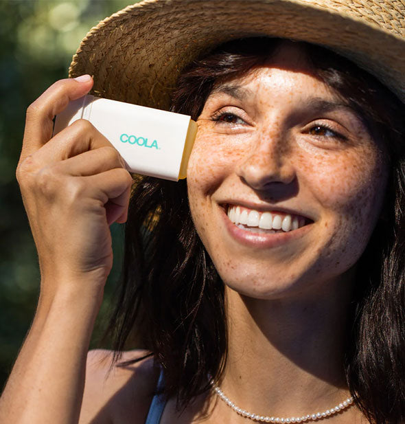 Smiling model applies Coola Classic Sunscreen Stick to cheek