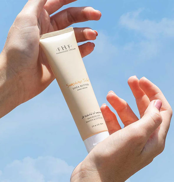 Model's hands hold a tube of FarmHouse Fresh Sunshine Silk Shea Butter Hand Cream in front of a blue sky
