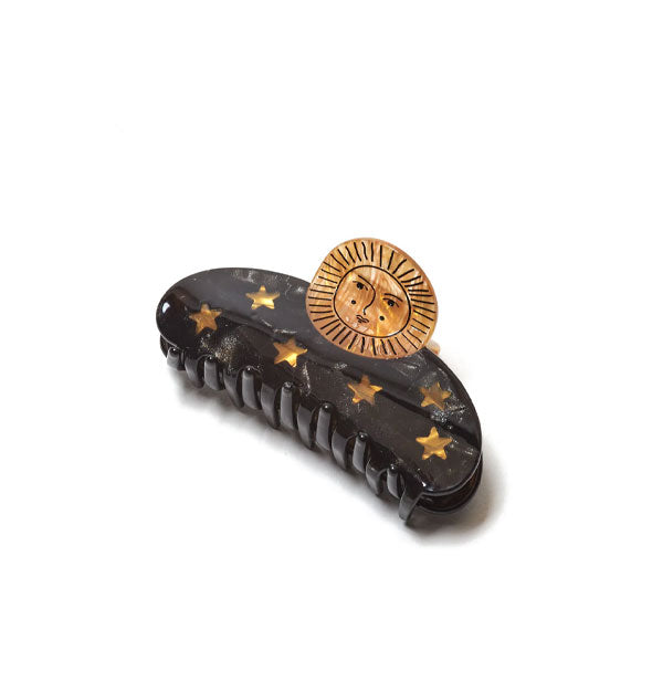 Claw clip with golden stars on a dark base topped with a golden stylized sun with face