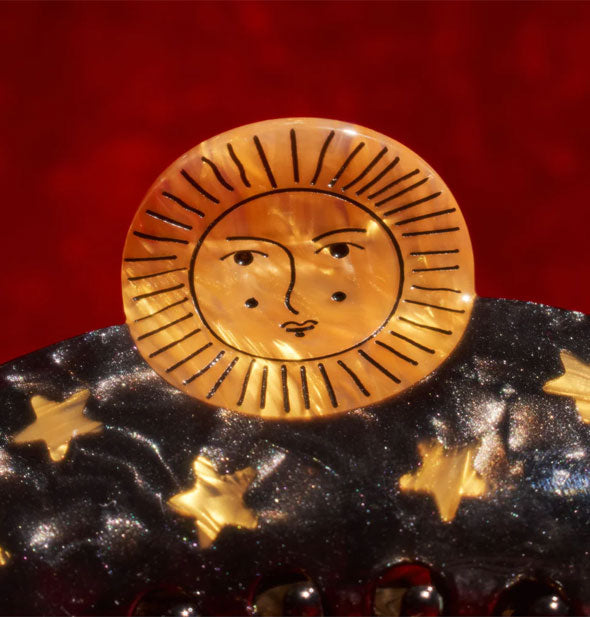 Closeup of claw clip's golden sun face and stars against a red backdrop